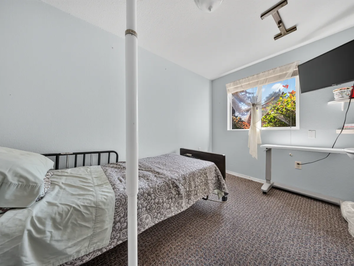 Resident bedroom with an adjustable bed and overbed table, set up for hospice care at A Care Of Joy