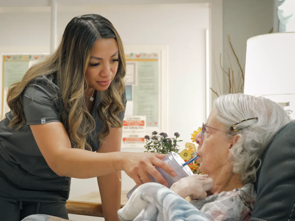 Caregiver helping a resident with a drink at A Care Of Joy adult family home